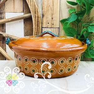 May include: A round, glazed terracotta casserole dish with a matching lid, featuring a warm brown finish and decorative patterns of small white and dark green dots arranged in circular motifs, complete with two side handles and a central lid handle.