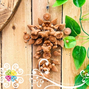 May include: A terracotta cross-shaped wall hanging, adorned with floral and leaf details. The cross features roses, daisies, and other stylized flowers. It hangs against a wooden background with a screw and twine for hanging.
