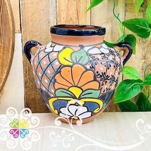 May include: A hand-painted ceramic vase with a wide body and two handles. The vase features a vibrant floral design in orange, yellow, blue, and white against a terracotta background. The rim and handles are dark blue. Decorative pottery.