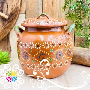 May include: A round terracotta clay pot with a matching lid and two side handles. The exterior features a hand-painted pattern of white, blue, and green dots arranged in floral and geometric motifs across the warm brown surface.
