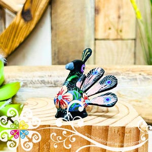 May include: A hand-painted black ceramic peacock figurine with a pink, blue, and green floral design. The peacock has its tail feathers spread out.