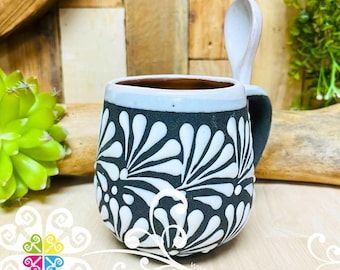 May include: A black and white ceramic mug with a floral design. The mug has a handle and a spoon.