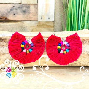 May include: A pair of vibrant red tassel earrings. Each earring features a fan-shaped design with a central ring adorned with colorful beads. The earrings hang from silver-colored hooks, offering a bold and eye-catching accessory.