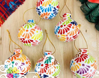Pode incluir: Sete enfeites de cerâmica pintados à mão com desenhos florais coloridos. Cada enfeite tem uma base branca e é adornado com padrões de flores vermelhas, laranja, amarelas, verdes, azuis e roxas. Laços dourados são anexados para pendurar.