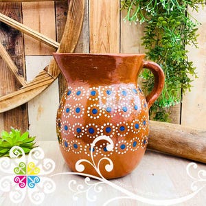 May include: A brown ceramic pitcher with a handle, decorated with white dots and blue circles. The pitcher has a wide mouth and a curved handle. The design is repeated around the body of the pitcher. The pitcher is likely used for serving beverages.