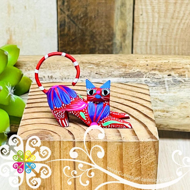 May include: A hand-painted wooden cat figurine with a red, white, and blue color scheme. The cat is lying down with its tail curled up. The figurine is on a wooden surface.