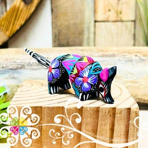 May include: A hand-painted wooden armadillo figurine with black, white, pink, blue, and green floral designs. The figurine is standing on a wooden surface.