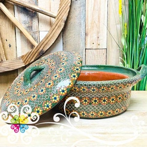 May include: Green ceramic casserole dish with a lid, both decorated with a white, orange, and black floral pattern. The dish has two handles.