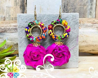 May include: Handmade earrings featuring vibrant pink rose-shaped pendants and colorful woven bead accents. The earrings have gold-colored metal hoops and hooks. The design incorporates a variety of bright colors, including pink, yellow, green, and blue.