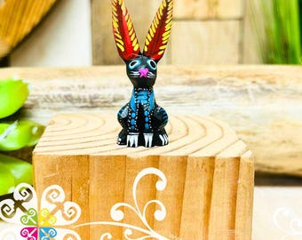 Pode incluir: Uma pequena figura de coelho de madeira pintada de preto, azul, amarelo e vermelho. O coelho tem orelhas compridas e um nariz rosa.