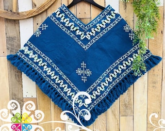 May include: A deep blue poncho featuring intricate white embroidered geometric patterns and floral motifs along the neckline and hem. The garment is finished with a fringe trim along the bottom edge and is displayed on a black hanger.