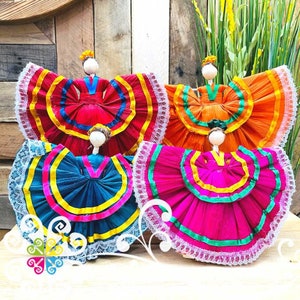 May include: Four handmade dolls wearing colorful dresses with layers of ruffles and lace. The dolls are made of straw and have a traditional Mexican folk art style.