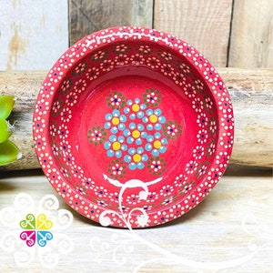 May include: A small red ceramic bowl with a white rim and a hand-painted design of a flower with blue, yellow, and green dots. The bowl is decorated with a pattern of white dots around the rim.