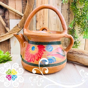 May include: Hand-painted terracotta teapot with a large handle and spout. The teapot features a floral design in red, blue, and yellow, with green and brown accents. The teapot has a lid and is suitable for serving tea.