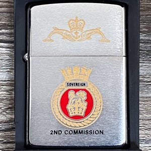 May include: A silver Zippo lighter in a black box. The lighter features a gold emblem with the text "SOVEREIGN" and "2ND COMMISSION". The box has the Zippo logo and the text "WORKS...OR WE FIX IT FREE".