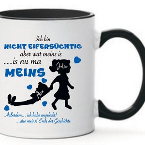 Könnte beinhalten: Weiße Keramiktasse mit schwarzem Rand und Henkel. Die Tasse zeigt eine schwarze Silhouette eines Mädchens, das einen Jungen an der Hand zieht. Der Text auf der Tasse lautet "Ich bin nicht eifersüchtig aber wat meins is...is nu ma MEINS" mit den Namen "Julia" und "Alex" auf dem Mädchen und dem Jungen. Der Text lautet auch "Außerdem...ich habs angeleckt!...also meins! Ende der Geschichte."