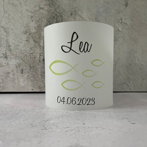 May include: White cylindrical candle holder with a green fish design and the name "Lea" and the date "04.06.2023" printed on it.