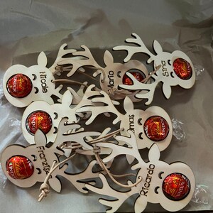 Puede incluir: Adornos de madera con forma de reno, grabados con nombres como Nicole, Mario, Sina, Franziska y Ricardo, cada uno con un chocolate Lindor. Los adornos est&aacute;n atados con cuerda.