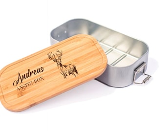 Puede incluir: Una fiambrera de madera con un recipiente de metal. La tapa es de madera y tiene un diseño de ciervo grabado. El texto "Andreas ANSITZ-BOX" también está grabado en la tapa.