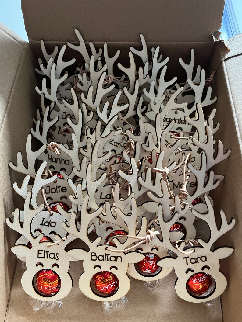 Puede incluir: Adornos navide&ntilde;os de renos de madera, cada uno con un nombre grabado en las astas. Las caras de los renos contienen bombones Lindt Lindor. Los adornos est&aacute;n en una caja de cart&oacute;n.