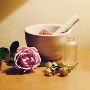 white mortar with flowers and an empty 50ml empty frosted glass bottle and a Lavender Rose bloom and buds without petals.