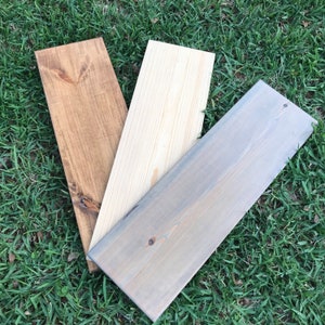 May include: Three wooden boards, one stained brown, one stained gray, and one left natural.