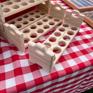 May include: Three light-colored wooden egg holders with multiple circular cutouts for storing eggs. Each holder features a rectangular base with side panels that include integrated handles at the top. The wood grain is visible throughout.