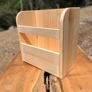 May include: A light-colored wooden organizer with a curved top and two horizontal dividers. The organizer is made of natural wood and has a rectangular shape. The wood grain is visible, and the piece appears to be handmade.