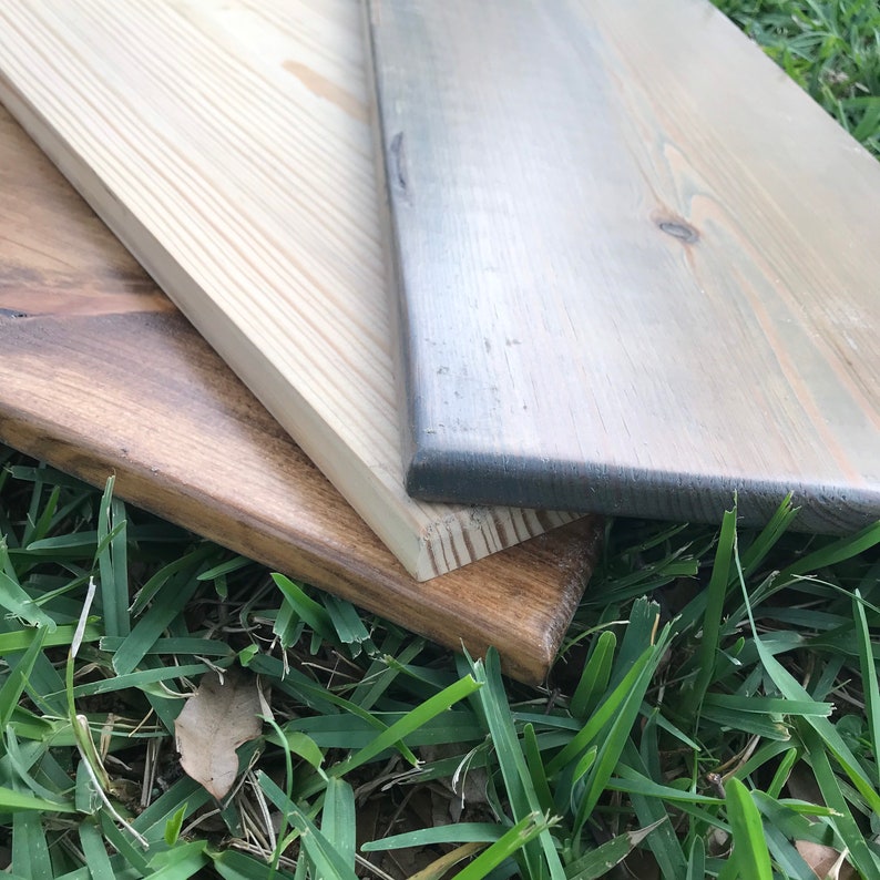 May include: Three wooden boards of different colors and textures. The top board is a light gray with a wood grain pattern. The middle board is a light brown with a smooth surface. The bottom board is a dark brown with a rough texture.