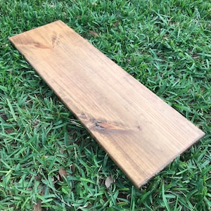 May include: A long, rectangular piece of wood with a natural wood grain finish. The wood has a light brown color and is smooth to the touch.