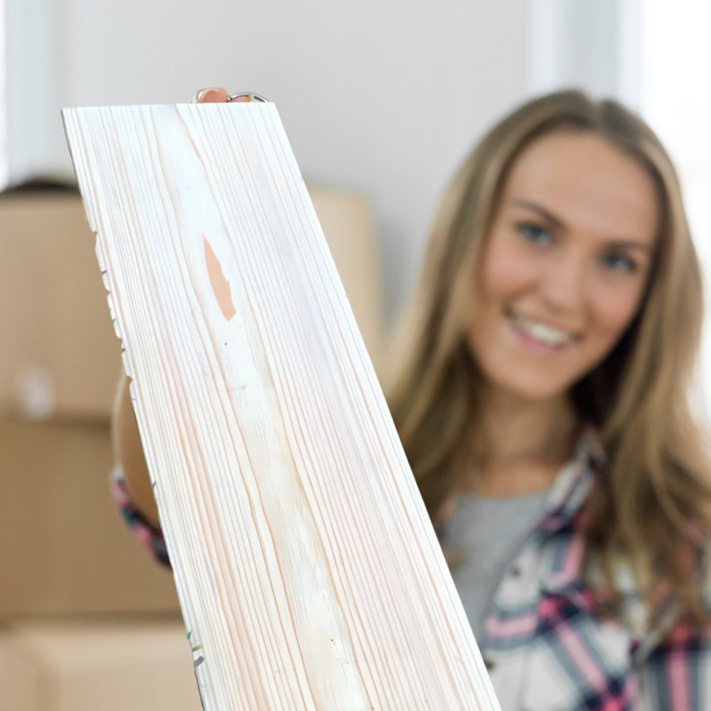 May include: A close-up of a white painted wood plank with visible grain. The plank is being held by a person out of focus in the background.