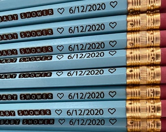 May include: A stack of light blue pencils with gold trim and pink erasers. Each pencil is personalized with the text "ALLIE'S BABY SHOWER" and the date "6/12/2020" in black.