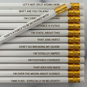 May include: A collection of white pencils with gold ferrules and erasers. Each pencil has a different science-themed phrase printed on it, such as "LET'S NOT SPLIT ATOMS HERE" and "THAT'S A FORCE TO BE RECKONED WITH". The pencils are arranged in a neat stack.