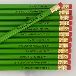 May include: Green pencils with gold metal bands and red erasers. Each pencil has a different pun printed in black, including "I'm Rooting For You" and "Let's Leaf Our Worries Behind". The pencils are arranged in a neat row.