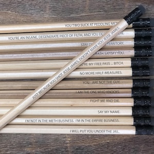 May include: A collection of wooden pencils with black erasers. Each pencil has a different quote printed in black ink. The pencils are arranged on a wooden surface.