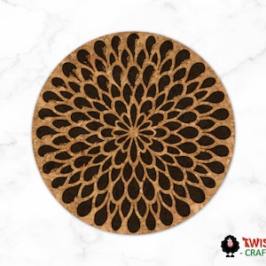 May include: Round cork coaster with a dark brown floral design. The coaster features a central flower-like pattern composed of teardrop shapes. The background is a light brown color, and the coaster is set against a white marble background.