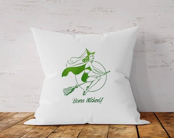 May include: White square pillow with a green illustration of a witch riding a broom inside a circle. The witch is wearing a hat and cape. The text "Born Wicked!" is below the illustration.