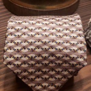 May include: A brown patterned silk tie with a geometric design featuring brown, beige, and blue colors.