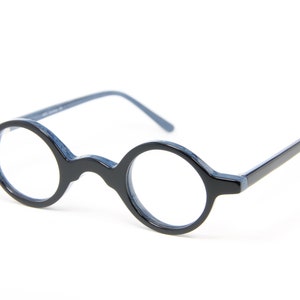 Könnte beinhalten: Schwarze Brille mit runden Gläsern und blauen Bügeln und Rahmen. Die Brille hat eine klassische, kreisförmige Linsenform und eine glänzende Oberfläche. Die Fassungen sind aus dunklem Material.