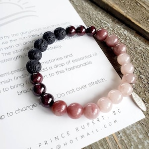 Op de afbeelding: Een veelkleurige edelsteen armband met zwarte lava kralen. De armband heeft een verloop van roze, rode en zwarte kralen. De armband ligt op een witte kaart met de tekst "Made in Prince Rupert, BC  TIALCOAST@HOTMAIL.COM".