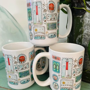 May include: Three white ceramic mugs featuring a repeating pattern of colorful postage stamp-style illustrations. The designs include a red and white lighthouse, green flip-flops, a bridge, a seagull, seashells, and a sign reading Welcome Beach Haven.