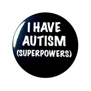 May include: A round, black button with white text that reads "I HAVE AUTISM (SUPERPOWERS)". The button has a glossy finish and a simple, bold design. The text is in a sans-serif font.