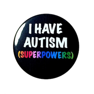 May include: A round, black button with the text "I HAVE AUTISM (SUPERPOWERS)" in white and rainbow colors. The button is glossy and has a simple, bold design.