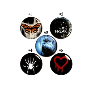 May include: Five round buttons with different designs. The first button has a butterfly with orange wings on a black and white background. The second button has the word "FREAK" in white letters on a black background. The third button has a blue and white owl on a dark background. The fourth button has a black spider on a white background. The fifth button has a red heart with dripping blood on a black background.