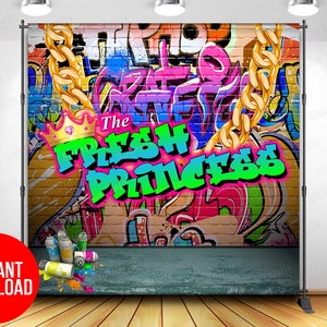 May include: A colorful backdrop featuring a brick wall with graffiti art, including the words "The Fresh Prince" in bright green and pink letters. A gold chain hangs from the top of the wall, and spray paint cans are scattered on the floor in front of the wall.