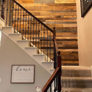 May include: A staircase with white risers, brown wooden handrails, and black iron balusters. The wall features a rustic wood paneling. A sign that says "home" is visible on the wall.