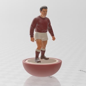 Può includere: Una statuetta di un calciatore in bordeaux e bianco in piedi su una base rossa e bianca. La statuetta è alta circa 7,5 cm.