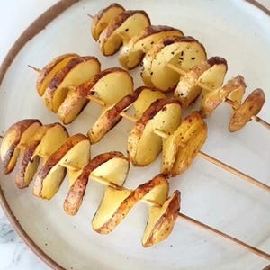 Può includere: Quattro spiedini di patatine fritte a spirale, dorate e croccanti, su un piatto bianco.