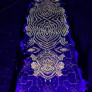 May include: A long, thin, black fabric with a glowing, neon green, pink, and yellow geometric pattern. The pattern is symmetrical and features intricate lines and shapes.