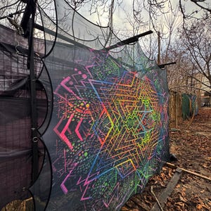 Może przedstawiać: Duży, czarny gobelin z siatki z żywym, geometrycznym wzorem w neonowych kolorach. Grafika przedstawia skomplikowane linie i kształty w kolorze różowym, zielonym, żółtym i niebieskim, tworząc efekt psychodeliczny. Gobelin jest wystawiony na zewnątrz, częściowo zasłaniając konstrukcję.